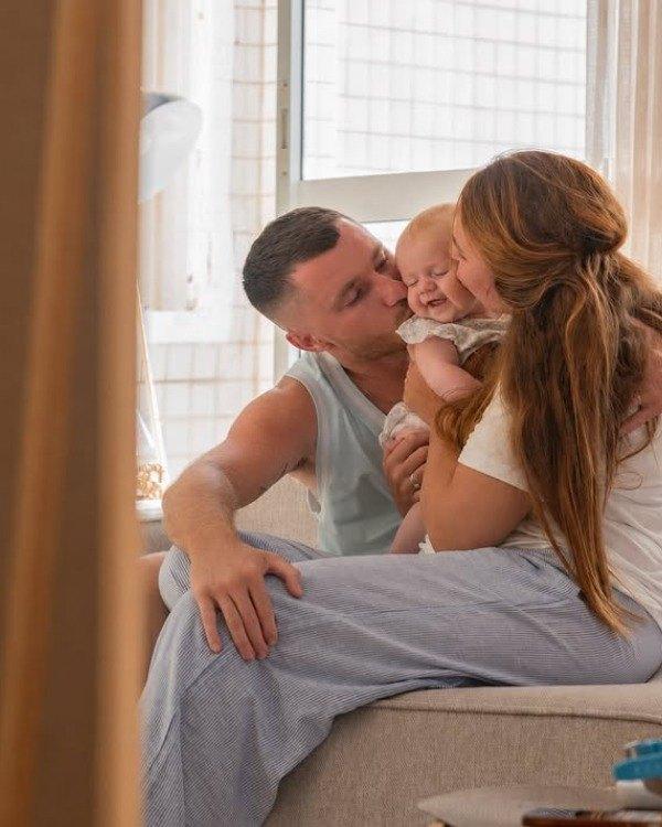 הורים מנשקים את התינוקת שלהם על הספה, בבית